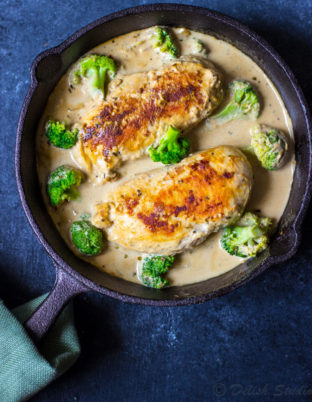 Creamy garlic chicken with broccoli in a skillet on a blue background