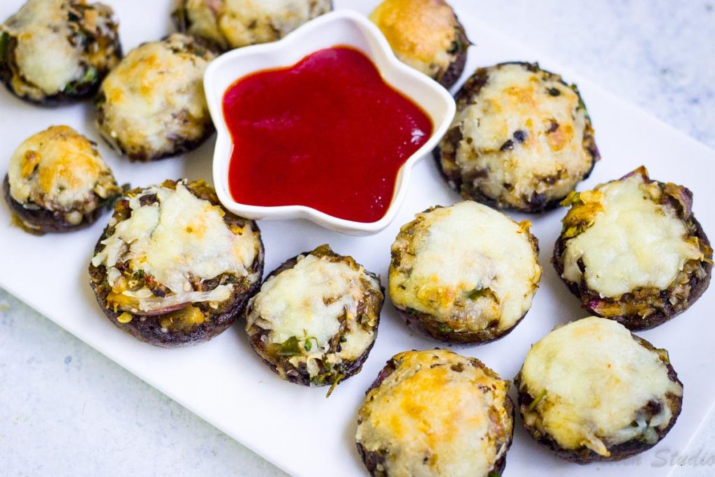 Vegetarian appetisers - cheese stuffed mushrooms on a white plate served with tomato ketchup.
